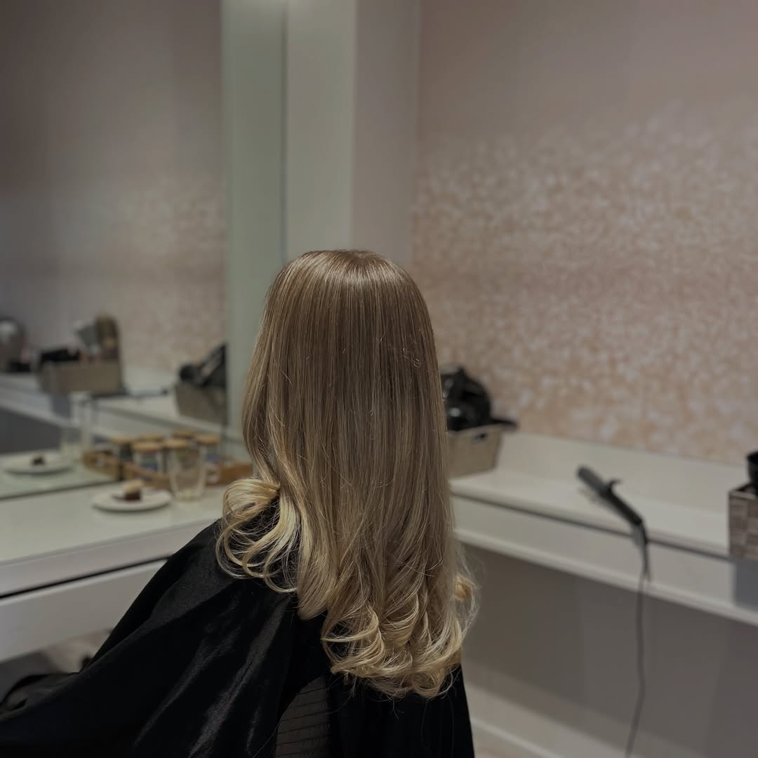Blond, gelaagd geföhnd haar met lichtere punten, voor de spiegelwand van de salon